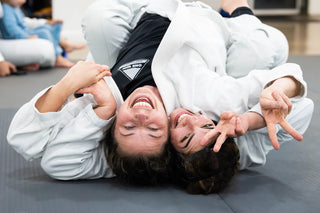 Two BJJ training partners laughing on the mat at One Way Martial Arts in Alexandria, VA
