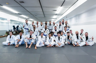Adult BJJ students and coaches in white gis posing for a team photo on the mats at One Way Martial Arts in Alexandria, VA