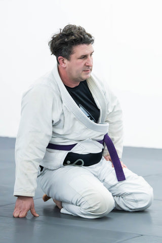 Adult BJJ purple belt student kneeling on the mat at One Way Martial Arts in Alexandria, VA