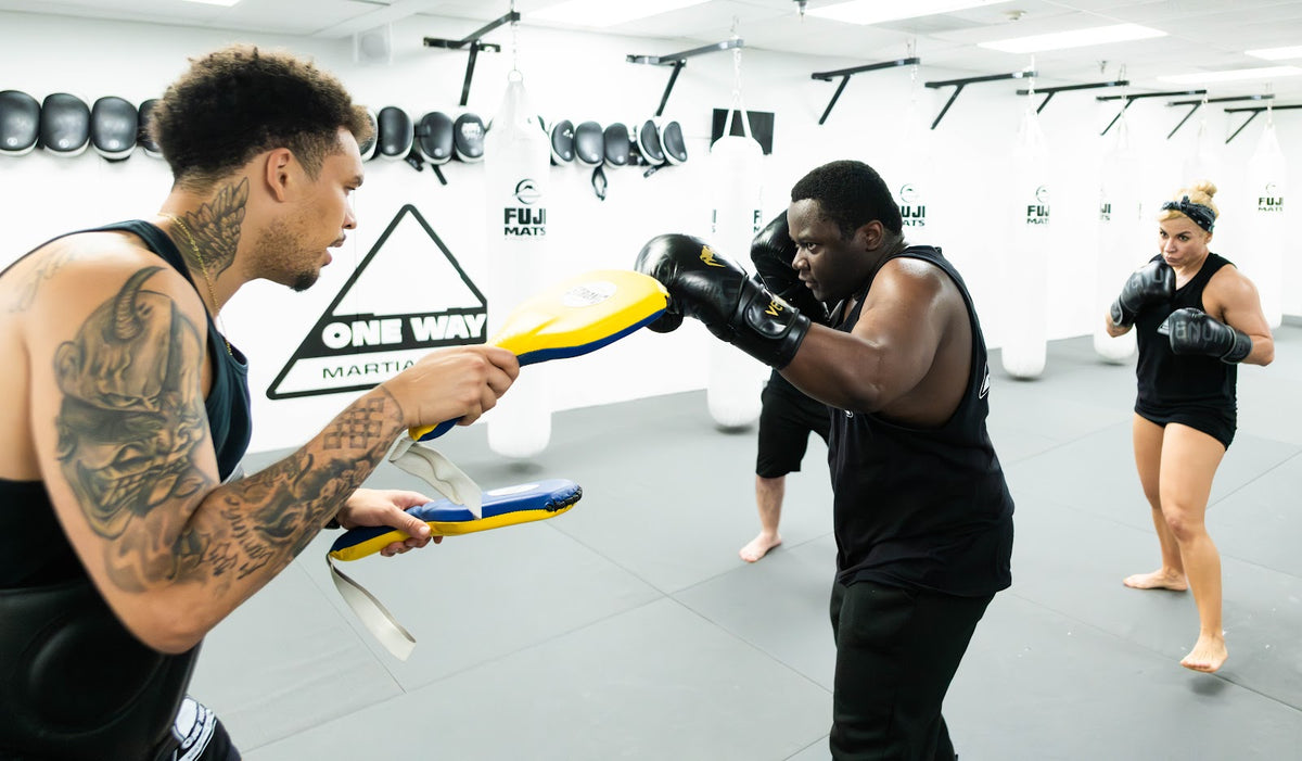 Coach holding Thai pads for a student during striking class at One Way Martial Arts in Alexandria, VA