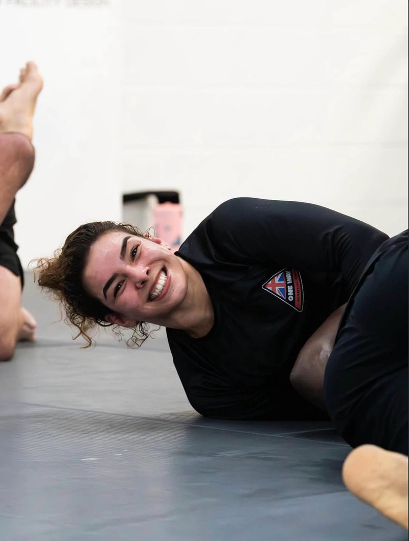 Coach Giovanna Amaral, IBJJF Pan American Champion and BJJ coach at One Way Martial Arts in Alexandria, VA, smiling during No-Gi training