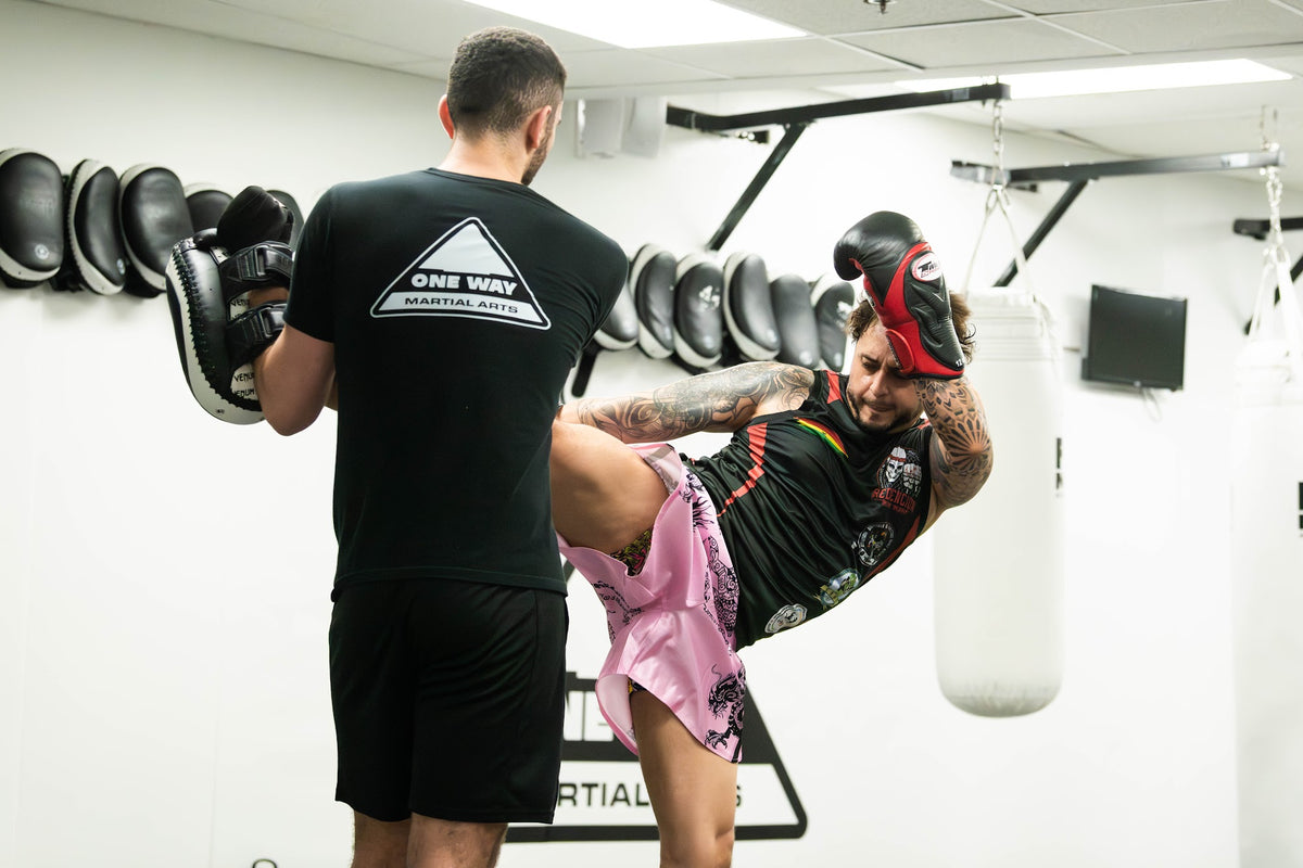 Coach holding pads for a Muay Thai kick at One Way Martial Arts in Alexandria, VA