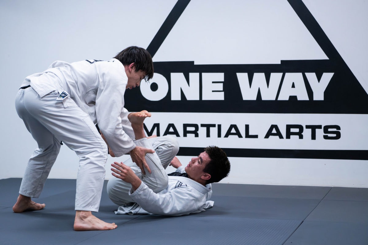 BJJ guard passing drill in front of the One Way Martial Arts logo wall in Alexandria, VA