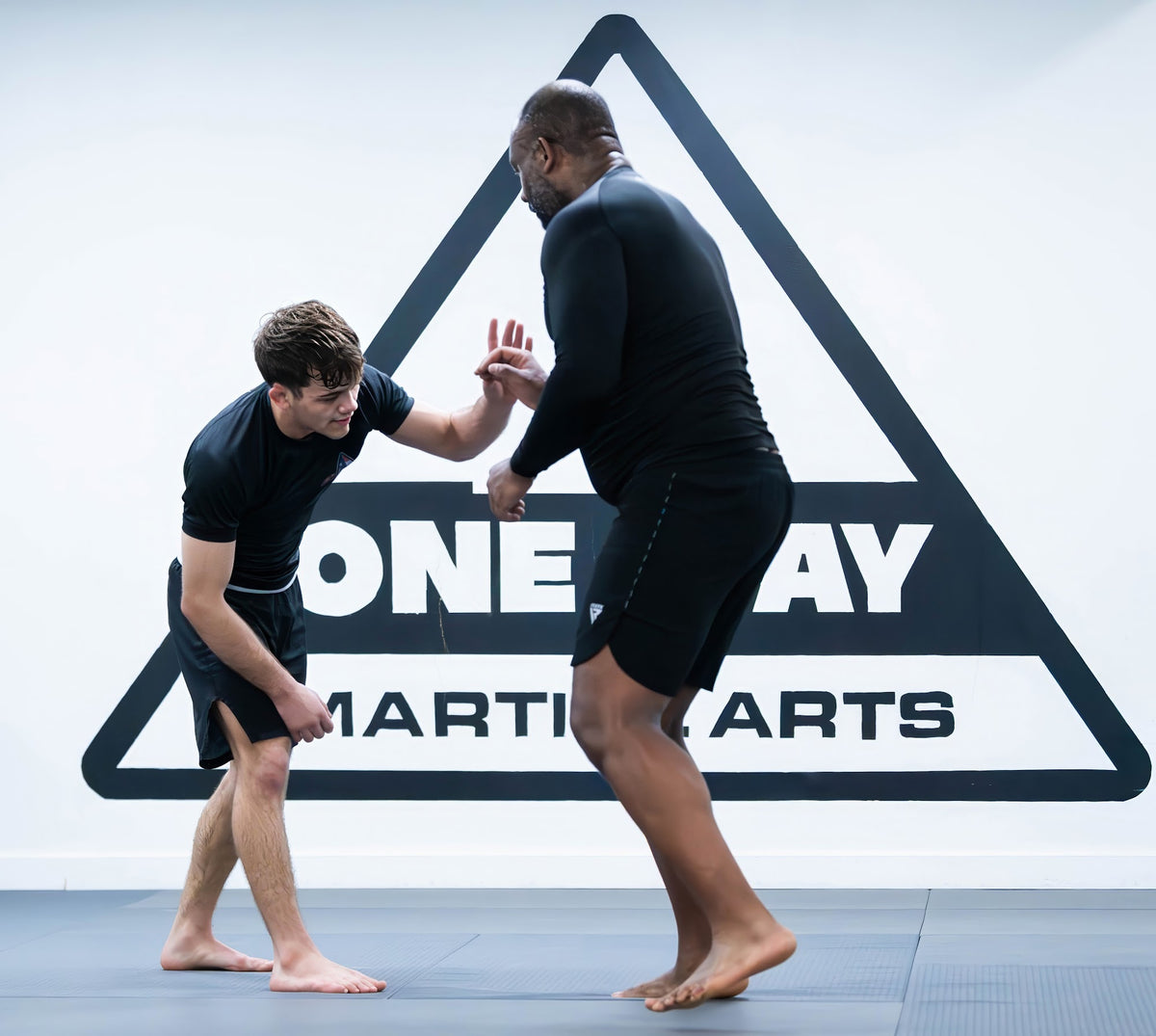 Two students drilling striking defense in front of the One Way Martial Arts logo in Alexandria, VA